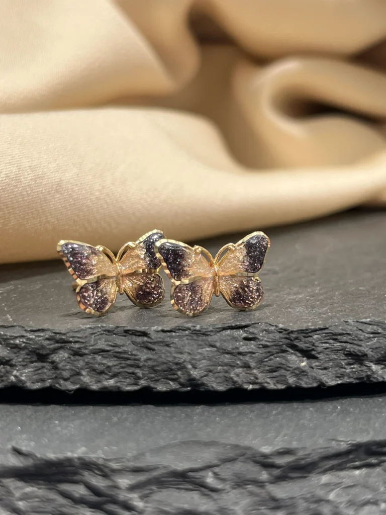 Złote kolczyki motyle na tle kamienia